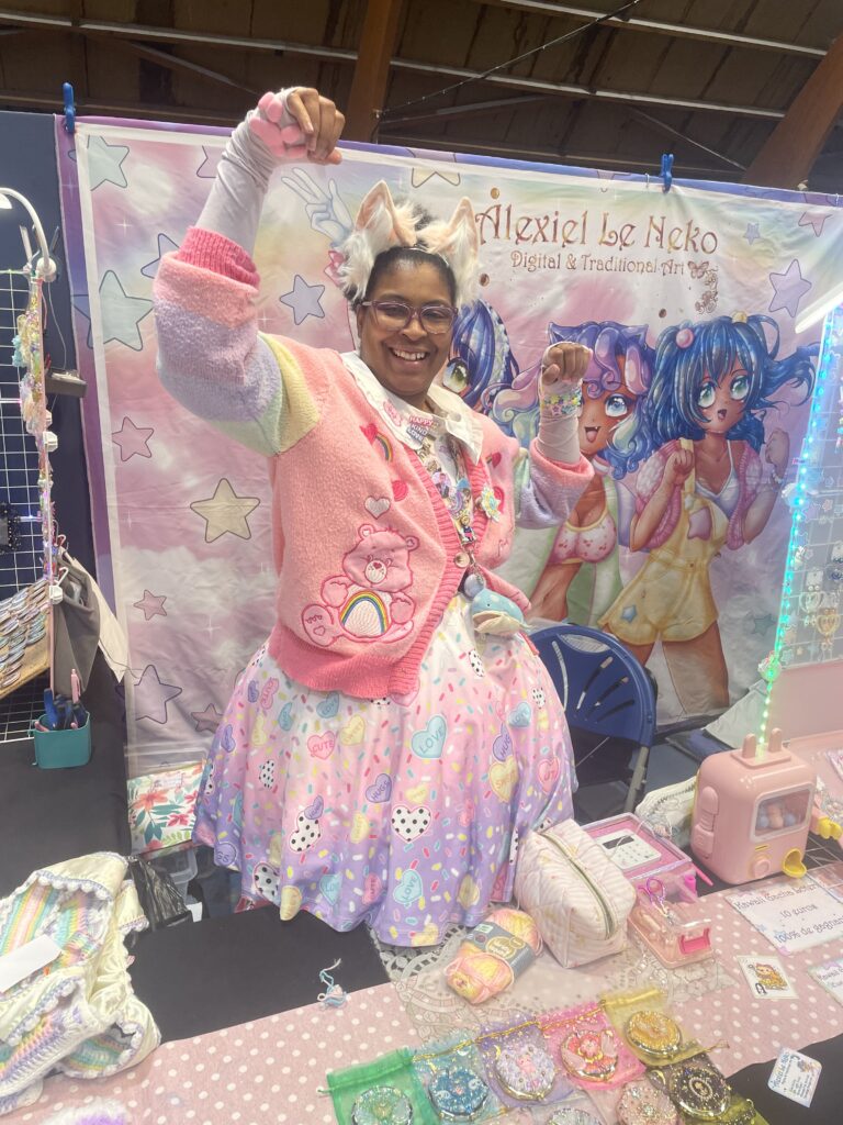 AlexielLeNeko en tenue Lolita devant son stand pastel